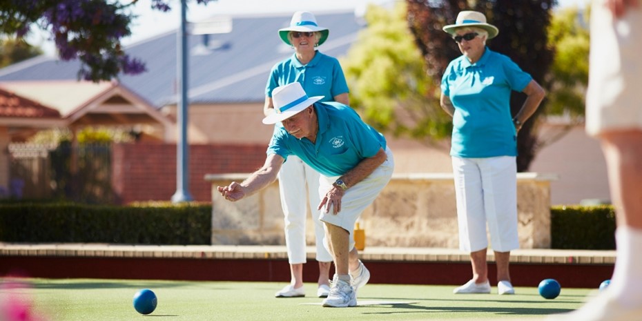 Elderly man playing lawn bowls with two women