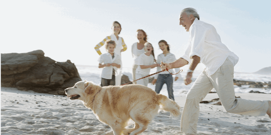 Man in white shirt running on beach with labrador dog