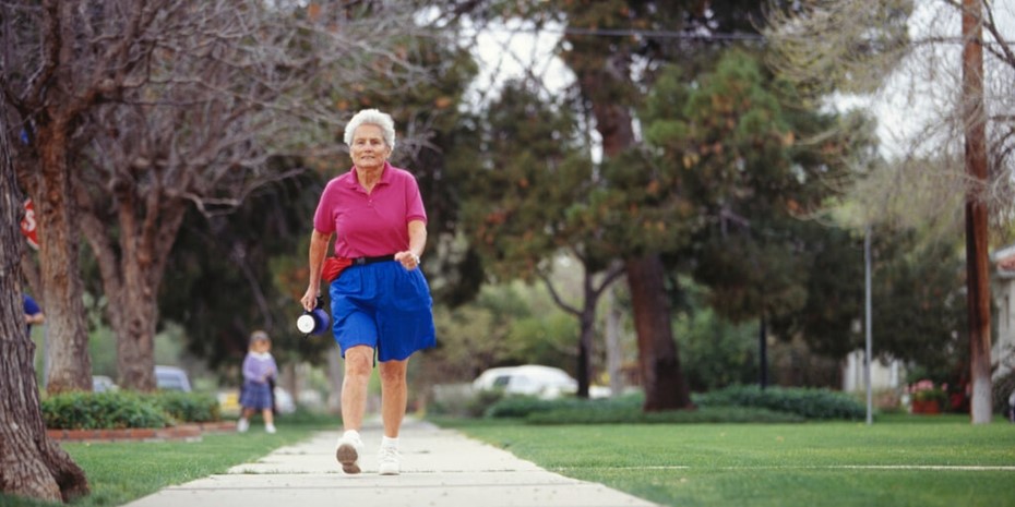 Elderly woman wearing pink shirt and blue shorts walking outside