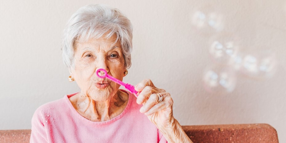 Elderly woman wearing pink shirt blowing bubbles