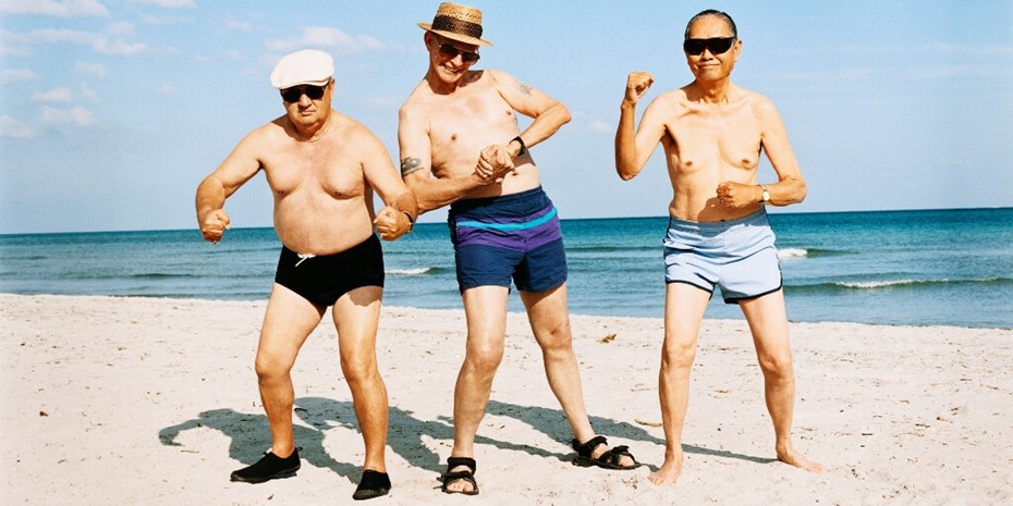 Three older men posing shirtless on beach