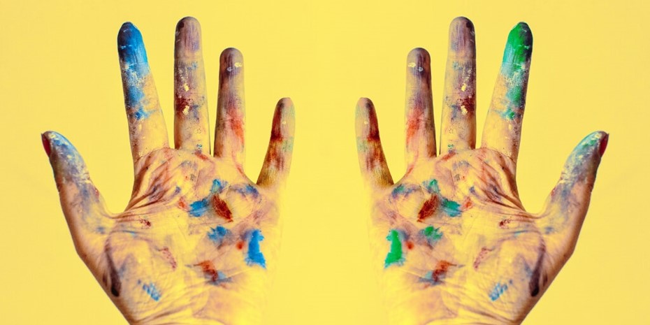 Two hands covered in multi-coloured paint on yellow background