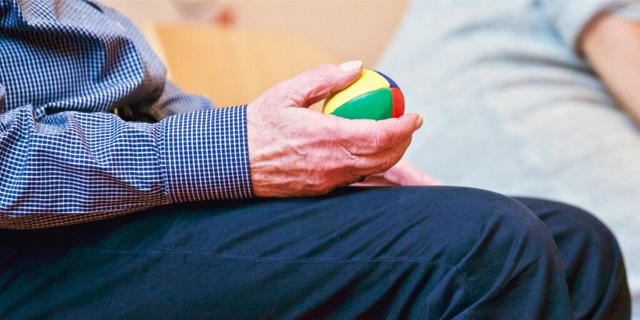 Close up of elderly man's hand holding a small multi-coloured ball