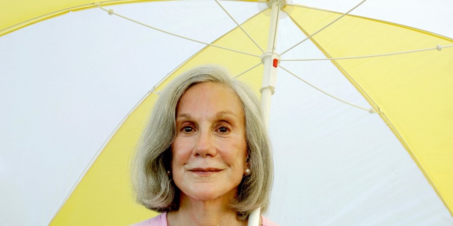 Elderly woman standing under yellow and white umbrella