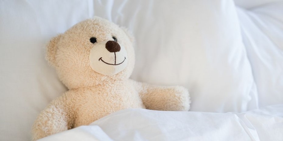 A teddy bear smiling laying in bed
