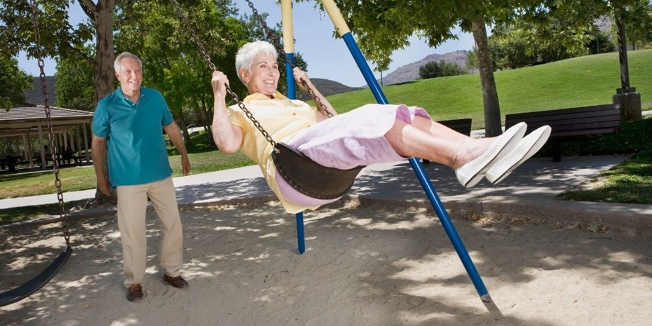 Elderly couple playing on a swing set at a park outside