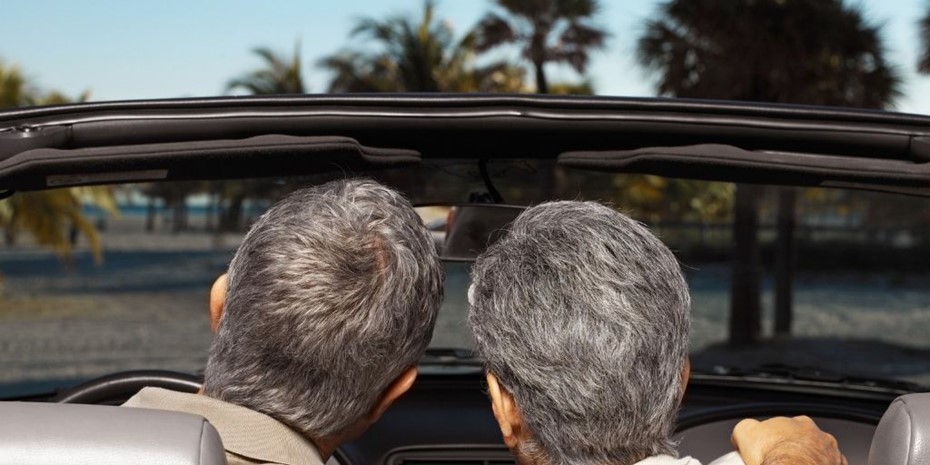 A close up of the back of the heads of an elderly couple with gray hair sitting in a convertible