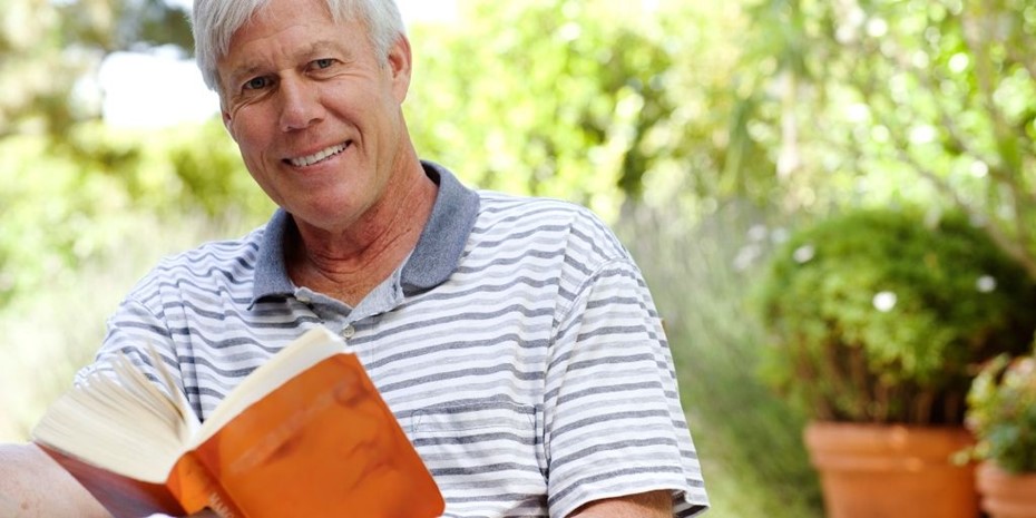 Elderly man with striped shirt reading a book outside