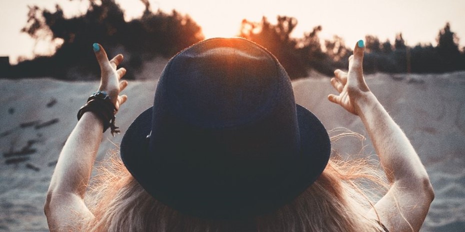 Woman wearing black hat with hands outstretched to a sunset
