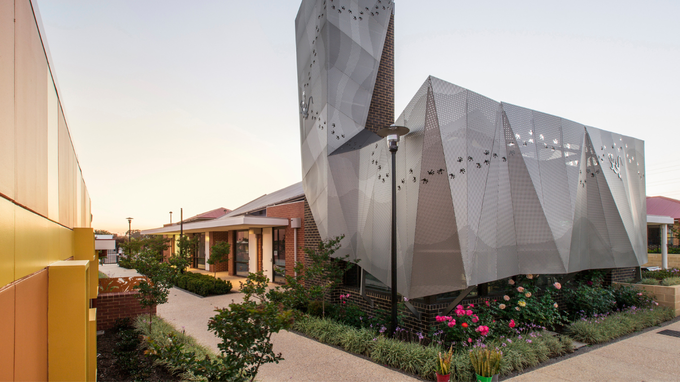 Brightwater Oats Street_wide view of architecturally designed metal structure building with native animal footprints and lizard with beautiful rose garden for disability clients