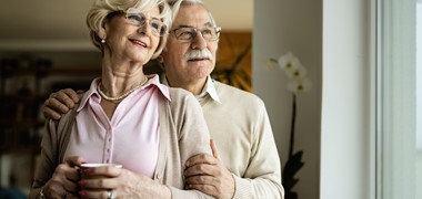 smiling-senior-couple-standing-embraced-looking-through-window.jpg