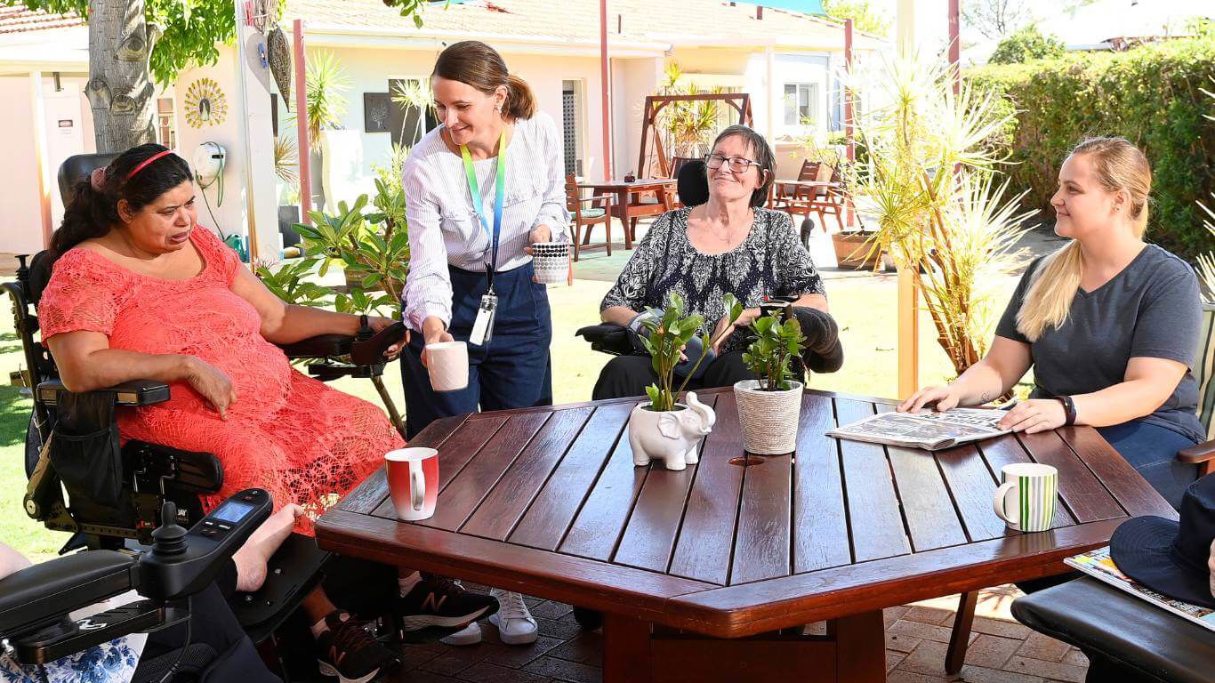 Brightwater Marangaroo Transitional Accommodation Program_disability clients sitting outside on a sunny day while worker gives them cup of tea