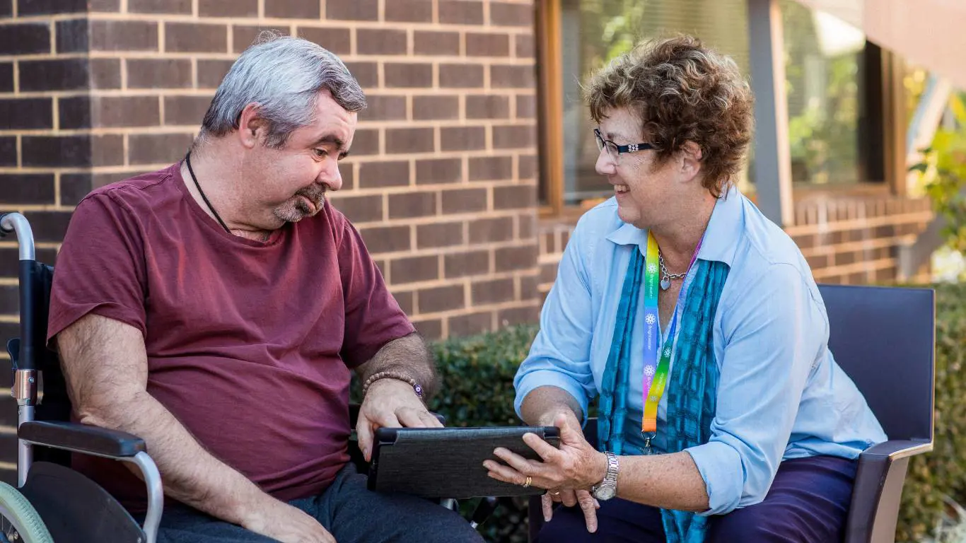 Brightwater Oats Street_showing disability client something on ipad outside in garden with brick external walls